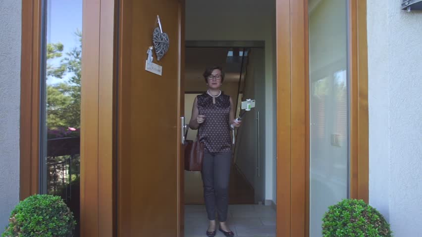 Casual outfit brunette woman in a brown blouse is standing in the doorway with phone. Licensed insurance agent recorded a video about meeting and assisting clients, answering questions about coverage. Royalty-Free Stock Footage #1018967230