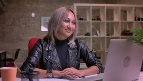 Amazing happy caucasian blonde woman is having energetic conversations on her laptop, video call illustration, while sitting in modern brick office isolated