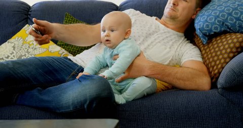 Father and baby boy watching television in living room at home Social distancing and self isolation in quarantine lockdown for Coronavirus Covid19