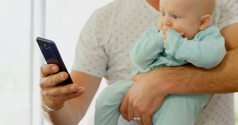 Close up of father and baby boy using mobile phone in living room at home Social distancing and self isolation in quarantine lockdown for Coronavirus Covid19