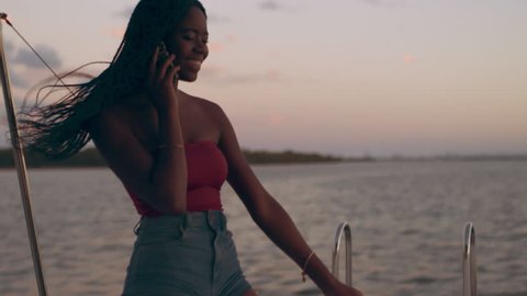 Young woman talking on her mobile phone while on a boat with a beautiful sunset in Australia. Medium close on 4k RED camera.