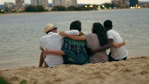 Two beautiful young couples cuddling on the beach get up and go. Wide shot from behind on 4K RED camera with shallow depth of field.