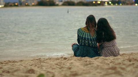 Two young women joined by their boyfriends who cuddle them on the beach, looking at the horizon at sunset. Wide shot from behind on 4K RED camera with shallow depth of field.