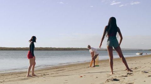 Friends casually playing cricket on the beach with sea and sun in the background in Australia. Wide shot on 4k RED camera.