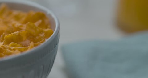Milk poured in a bowl of cereal, on a white table with a cup of coffee. Close up in slow motion with a shallow depth of field in 4K on a Phantom Flex camera.