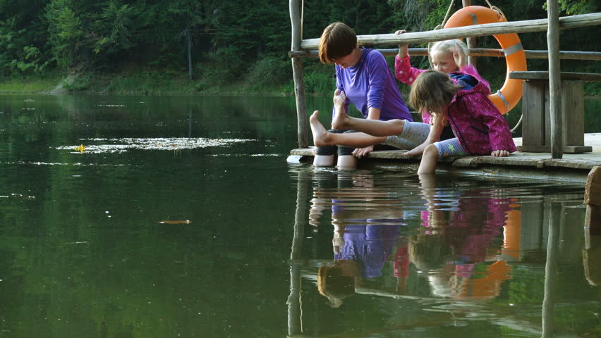 children sitting on a lake shore with their feet in the water
