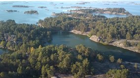 Stunning aerial view from the Swedish archipelago. Beautiful sunny summer day in Sweden. Drone flies forward over a forest on a tiny island. Camera slowly tilts down. Beautiful Scandinavian scenery.