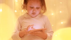 Little girl looking on the smartphone screen and playing in the downloaded application.