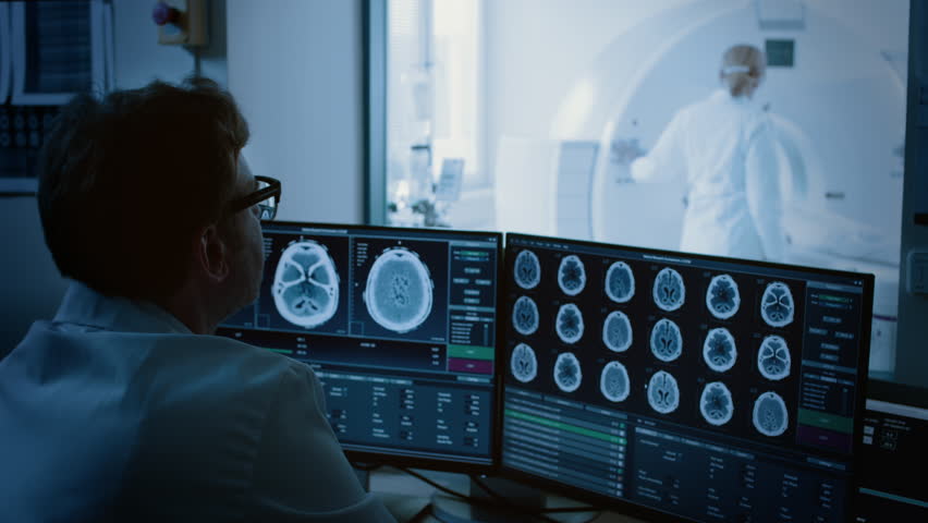 In Medical Laboratory Patient Undergoes MRI or CT Scan Process under Supervision of Radiologist, in Control Room Doctor Watches Procedure and Monitors with Brain Scans Results. Royalty-Free Stock Footage #1019002372