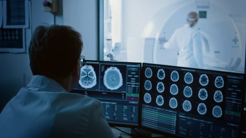 In Medical Laboratory Patient Undergoes MRI or CT Scan Process under Supervision of Radiologist, in Control Room Doctor Watches Procedure and Monitors with Brain Scans Results.