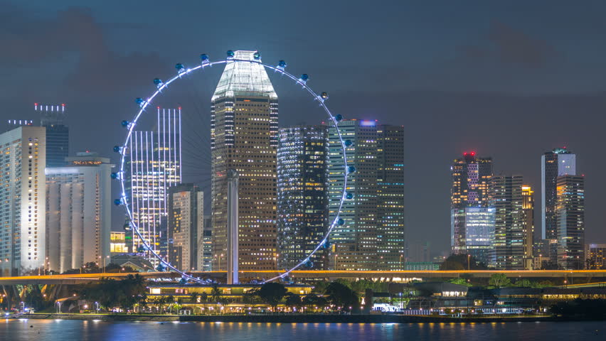 Skyline of Singapore with famous Singapore Ferries Wheel at night timelapse. Illuminated skyscrapers on a background