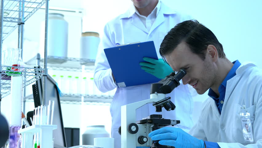 Scientist is looking through microscope with colleagues working in modern laboratory or medical center together. Concept of science, testing development and lab industry. Royalty-Free Stock Footage #1019008372