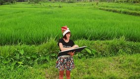 Happy New Year 2019. 4K flying drone video of young woman with santa hat and whiteboard with handwritten text posing among green rice field on Bali island.