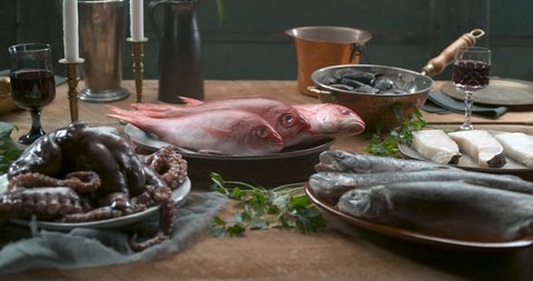 Various types of fresh fish, octopus and muscles arranged on plates and in bowls on a wooden table in slow motion, in soft lighting. Medium to closeup shot in 4k at 1000 fps on a Phantom Flex camera