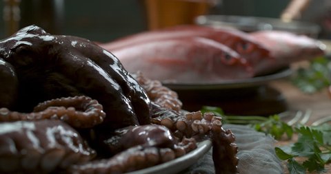 Various types of fresh fish, octopus and muscles arranged on plates and in bowls on a wooden table with candles and glasses of red wine in soft lighting. Closeup shot in 4k on a Phantom Flex camera