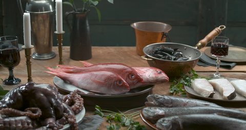 Various types of fresh fish, octopus and muscles arranged on plates and in bowls on a wooden table in soft lighting. Medium shot in 4k at 1000 fps on a Phantom Flex camera