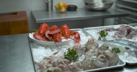 Hands place fresh fish with a variety of other fish, seafood, muscles, crawfish, lobsters and other shellfish arranged in trays of ice in soft light. Medium shot in 4k at 1000 fps on a Phantom Flex