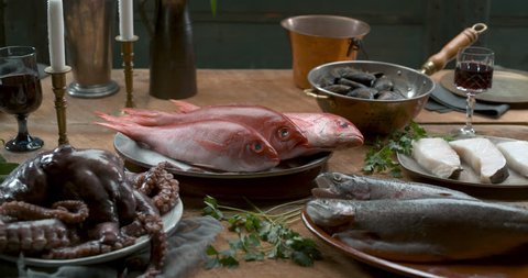 Hands place fresh fish on a metal plate with various types of other fish, octopus and muscles arranged on plates and in bowls on a wooden table in soft lighting. Medium shot in 4k on a Phantom Flex