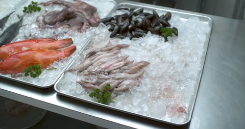 Hands place fresh fish with a variety of other fish, seafood, muscles, crawfish, lobsters and other shellfish arranged in trays of ice in soft light. Medium shot in 4k at 1000 fps on a Phantom Flex