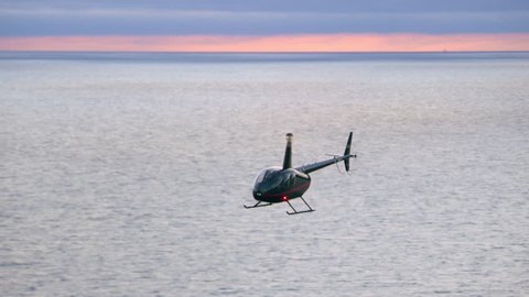 Aerial view of helicopter flying over ocean shoreline city with mountains in the distance during purple and pink sunset in Los Angeles, California. Wide long shot on 4K RED camera.