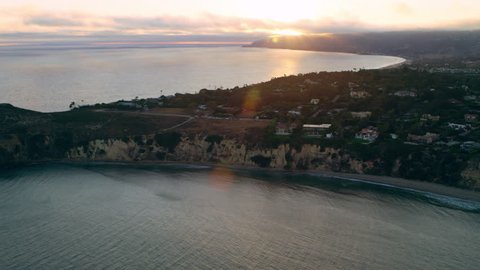 Aerial view of helicopter flying over ocean shoreline city with mountains in the distance during purple sunset in Los Angeles, California. Wide long shot on 4K RED camera.