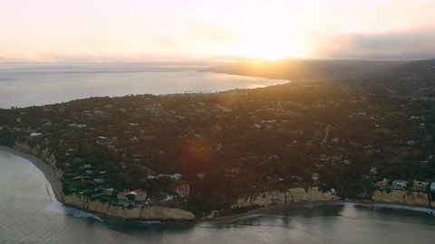 Aerial view of helicopter flying over ocean shoreline city with mountains in the distance during magical sunset in Los Angeles, California. Wide long shot on 4K RED camera.