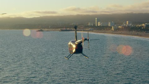 Aerial view of helicopter flying over ocean shoreline near pier during beautiful sunset in Los Angeles, California. Wide long shot on 4K RED camera.