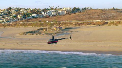 Aerial view of helicopter flying over Malibu beach during golden hour in Los Angeles, California. Wide long shot on 4K RED camera.