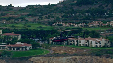 Aerial view of helicopter flying near ocean over cliff side mountain houses during a beautiful sunset in Los Angeles, California. Wide long shot on 4K RED camera.