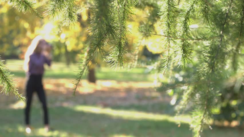 Charming girl in park.
Girl stands with photo camera in the park. She takes pictures on nature and is building the frame carefully. Wind blows, people go on back. Defocus with the foreground.