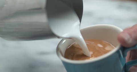 Barista making latte milk design by pourring milk in blue cup closeup with 4k Phantom Flex camera