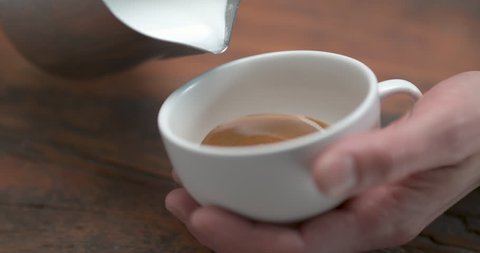 Barista making latte by pourring milk in white cup in closeup with 4k Phantom Flex camera