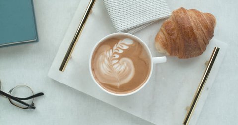 Pretty latte leaf design in white cup next to butter croissant and reading glasses ultra slow motion closeup with 4k Phantom Flex camera