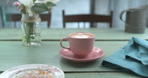 Pretty pink latte cup next to empty plate of eaten croissant and napkin ultra slow motion closeup