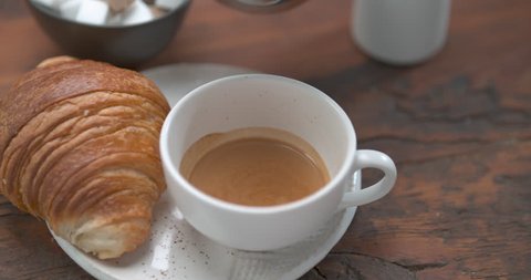 Mouth watering latte being poured in cup next to butter croissant closeup