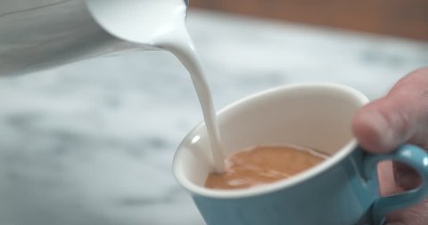 Close up shot of barista making latte art by pourring milk in blue coffee cup. Shot in ultra slow motion with 4k Phantom Flex camera