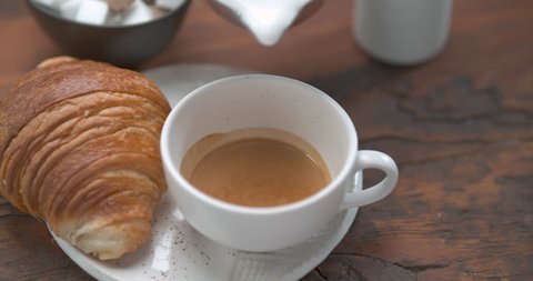 Savory latte being poured in coffee cup next to butter croissant ultra slow motion closeup with 4k Phantom Flex camera