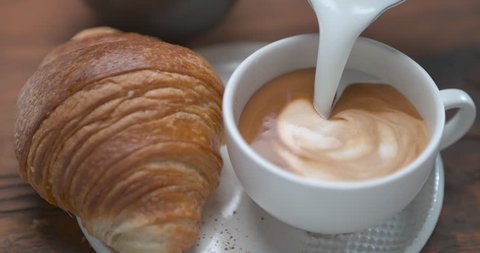 Milk froth poured in a nice coffee cup to make a latte next to butter croissant ultra slow motion closeup with 4k Phantom Flex camera