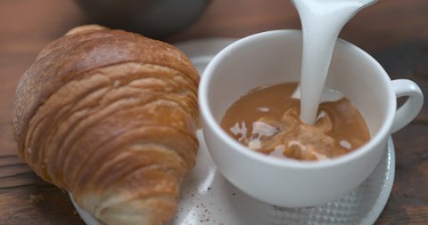 Mouth watering latte being poured in cup next to butter croissant ultra slow motion closeup with 4k Phantom Flex camera.
