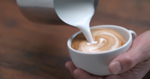 Barista making latte by pourring milk in white cup in ultra slow motion closeup with 4k Phantom Flex camera