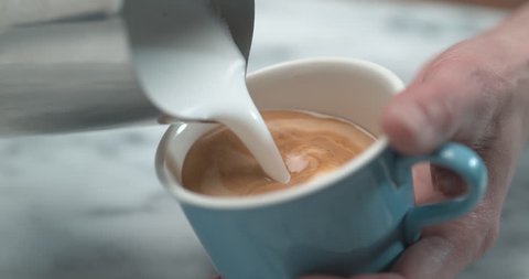 Barista making latte milk design by pourring milk in blue cup in ultra slow motion closeup with 4k Phantom Flex camera