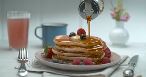 Maple syrup is poured over a stack of pancakes with fruit and butter on table in slow motion. Chef's Table, cooking show and Food Network inspired footage. Closeup shot in 4K on a Phantom Flex