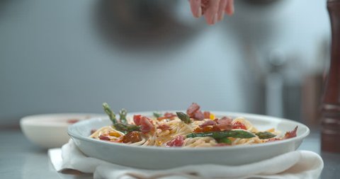 Hand dropping Italian pancetta onto spaghetti primavera dish in bowl in ultra slow motion with 4k Phantom Flex camera