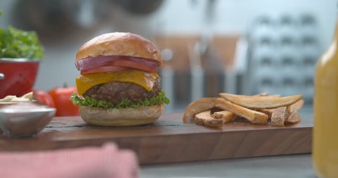 Crispy french fries dropping next to juicy cheeseburger on plate with sauce in ultra slow motion with 4k Phantom Flex camera