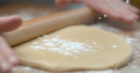 Sprinkled flour drops onto dough being rolled with rolling pin, in soft focus, in soft light, in slow motion. Closeup shot in 4K on Phantom Flex.
