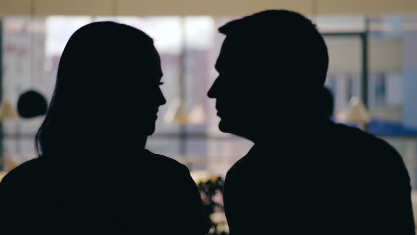 silhouettes of man and woman are talking at a table in the cafe and drinking drinks on the background of the window. Blurred background