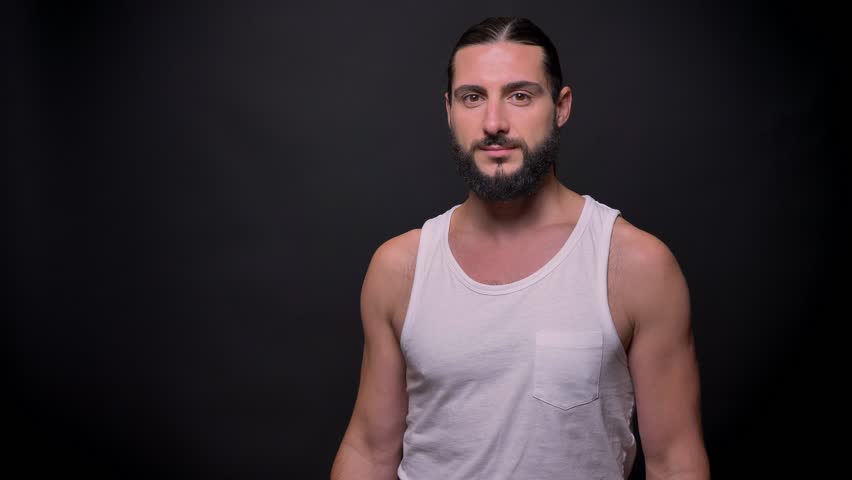 Perfect muscular arm of healthy strong caucasian man with beard and long black hair, who is standing and looking at camera directly while being indoor, good shape