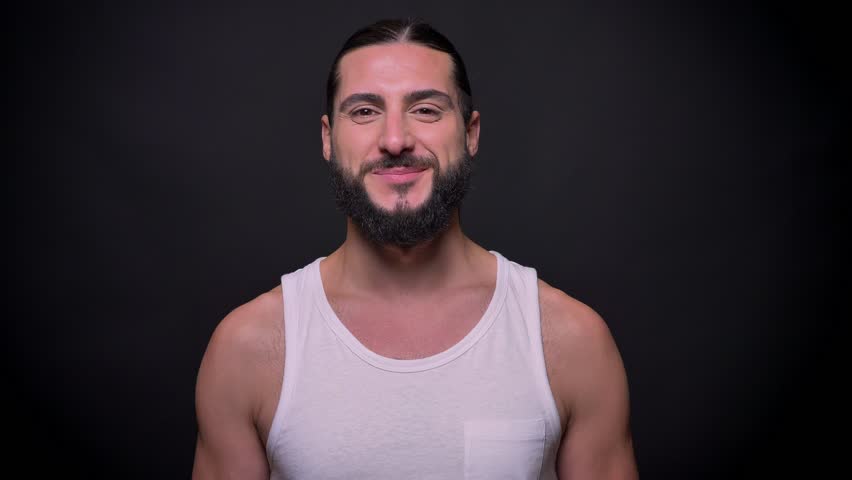 Awesome smiling man with perfect fit body and beard is standing on black background alone and smiling happily at camera, focused handsome person