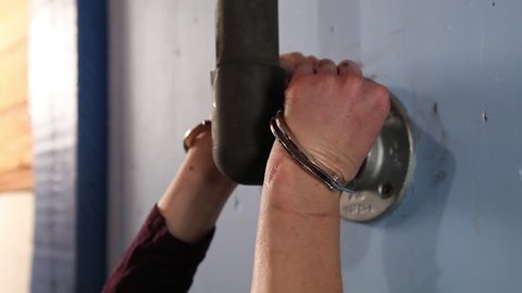 Side close-up shot of presumably female hands handcuffed around a pipe sticking out of the wall.