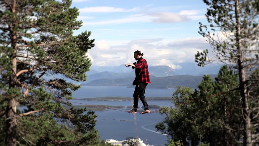 Slow motion shot of man walking and keeping balance on slackline in the mountains, beautiful view over Norway, Europe.